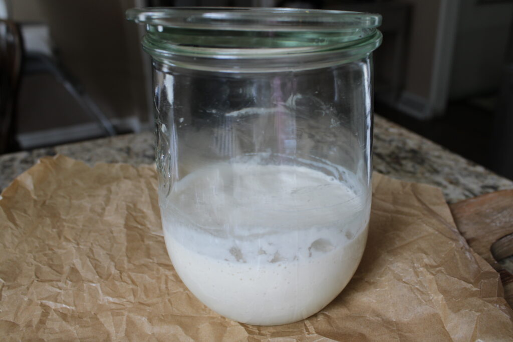 Fresh sourdough starter in glass jar on wooden cutting board.