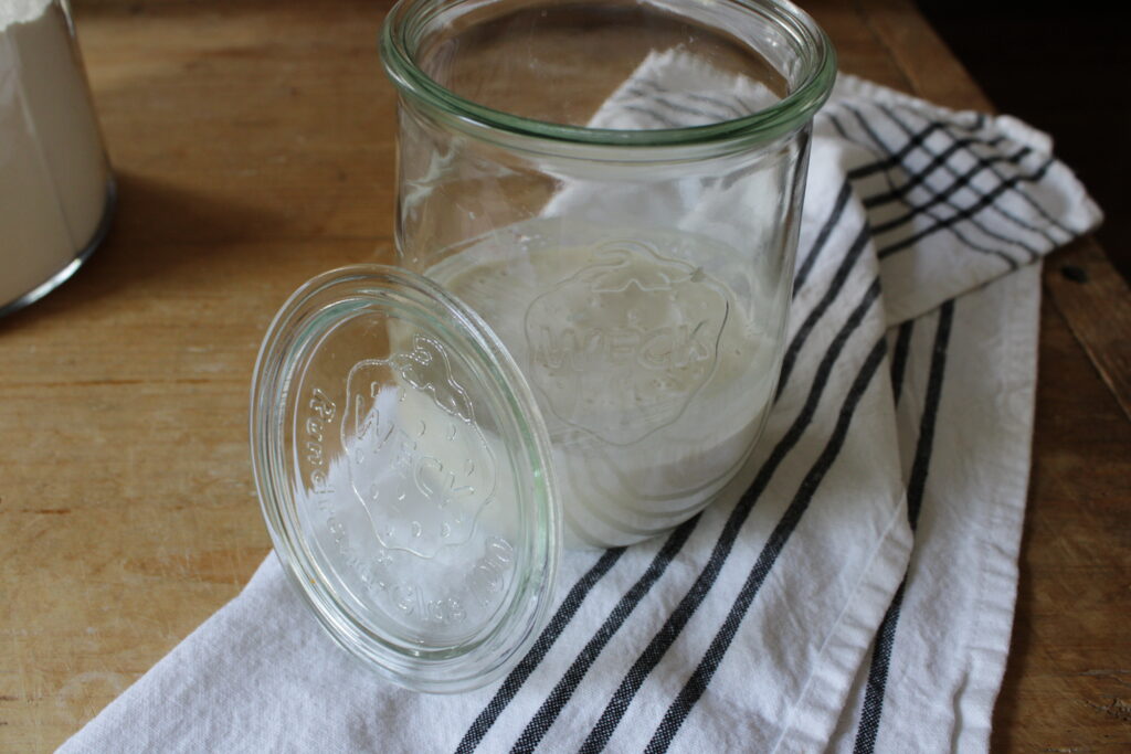 Jar of fresh homemade sourdough starter with blue and white striped tea towel underneath.